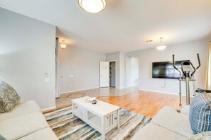 A spacious living room with a large TV, exercise bike, and a white coffee table.