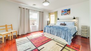 Een slaapkamer met een bed, een stoel, een nachtkastje, een lamp en een raam met gordijnen.