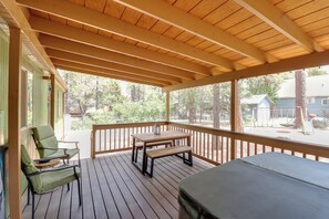 Una terrazza coperta all'aperto con tavolo e sedie di legno, una panca e vista sugli alberi e le case circostanti.