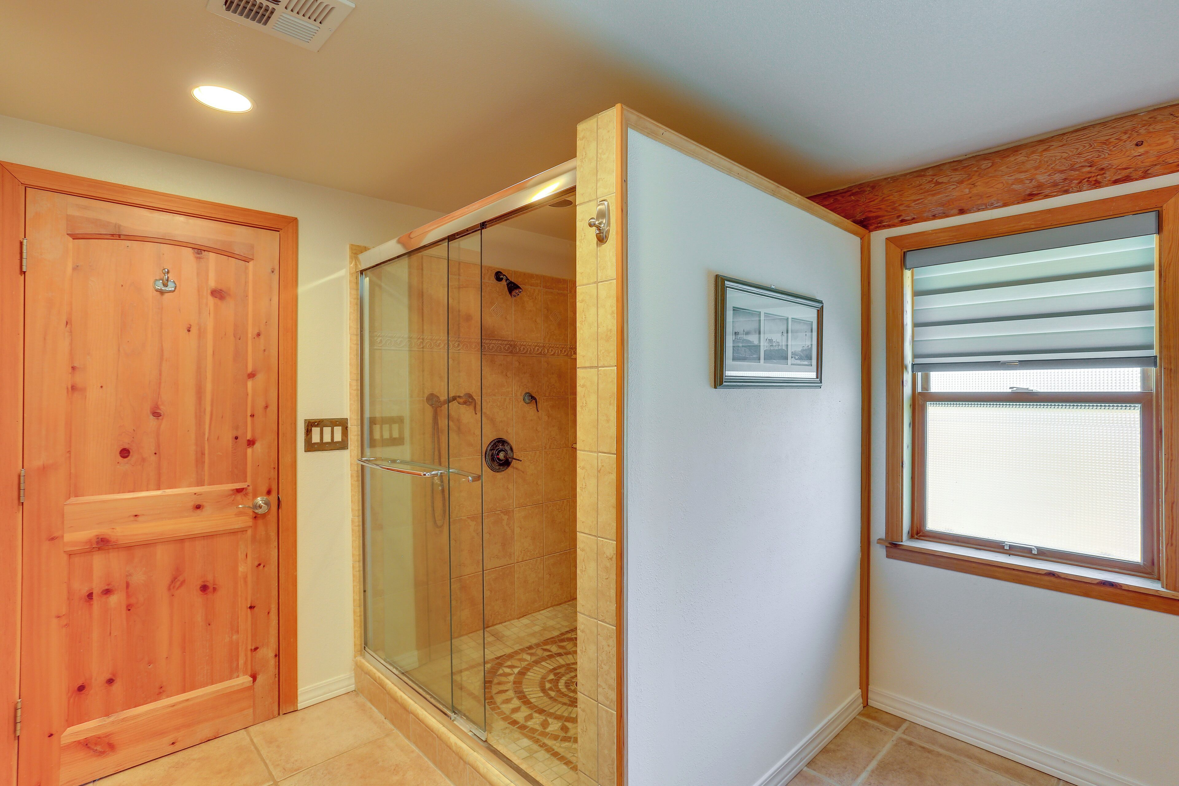 A bathroom with a wooden door, a glass shower enclosure, and a window with blinds.