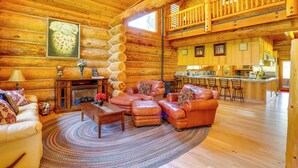 L’intérieur d’une cabane en rondins comprend un salon, une cheminée, des canapés en cuir et un coin cuisine.