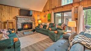 A cozy living room with a stone fireplace, wooden walls, and a large window. - Mtn Getaway w/ Indoor Hot Tub, Golfers Welcome! (White Haven)