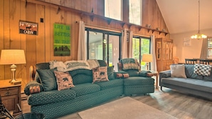 A cozy cabin interior with a green sofa set, a grey sofa, and a dining table. There are signs on the walls, a chandelier, and a large window. - Mtn Getaway w/ Indoor Hot Tub, Golfers Welcome! (White Haven)