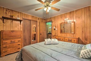 A wooden-paneled bedroom with a bed, dresser, and ceiling fan.