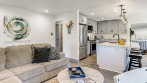 A modern living room with a sofa, a coffee table, and a kitchen area with a refrigerator, microwave, and island. - Relax Fireside: Prescott Retreat w/ Hot Tub! (Prescott)