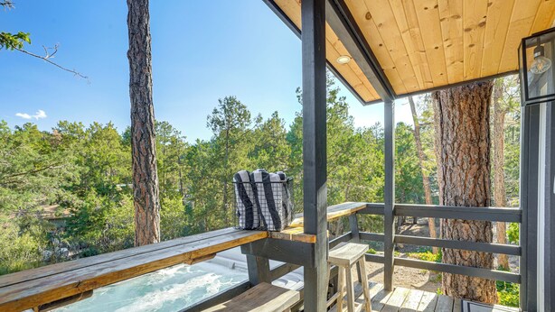 A wooden deck with a hot tub, benches, and a view of a forest. - Relax Fireside: Prescott Retreat w/ Hot Tub! (Prescott)