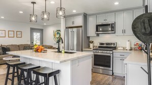 A modern kitchen with a central island, stainless steel appliances, and a dining area with bar stools. - Relax Fireside: Prescott Retreat w/ Hot Tub! (Prescott)