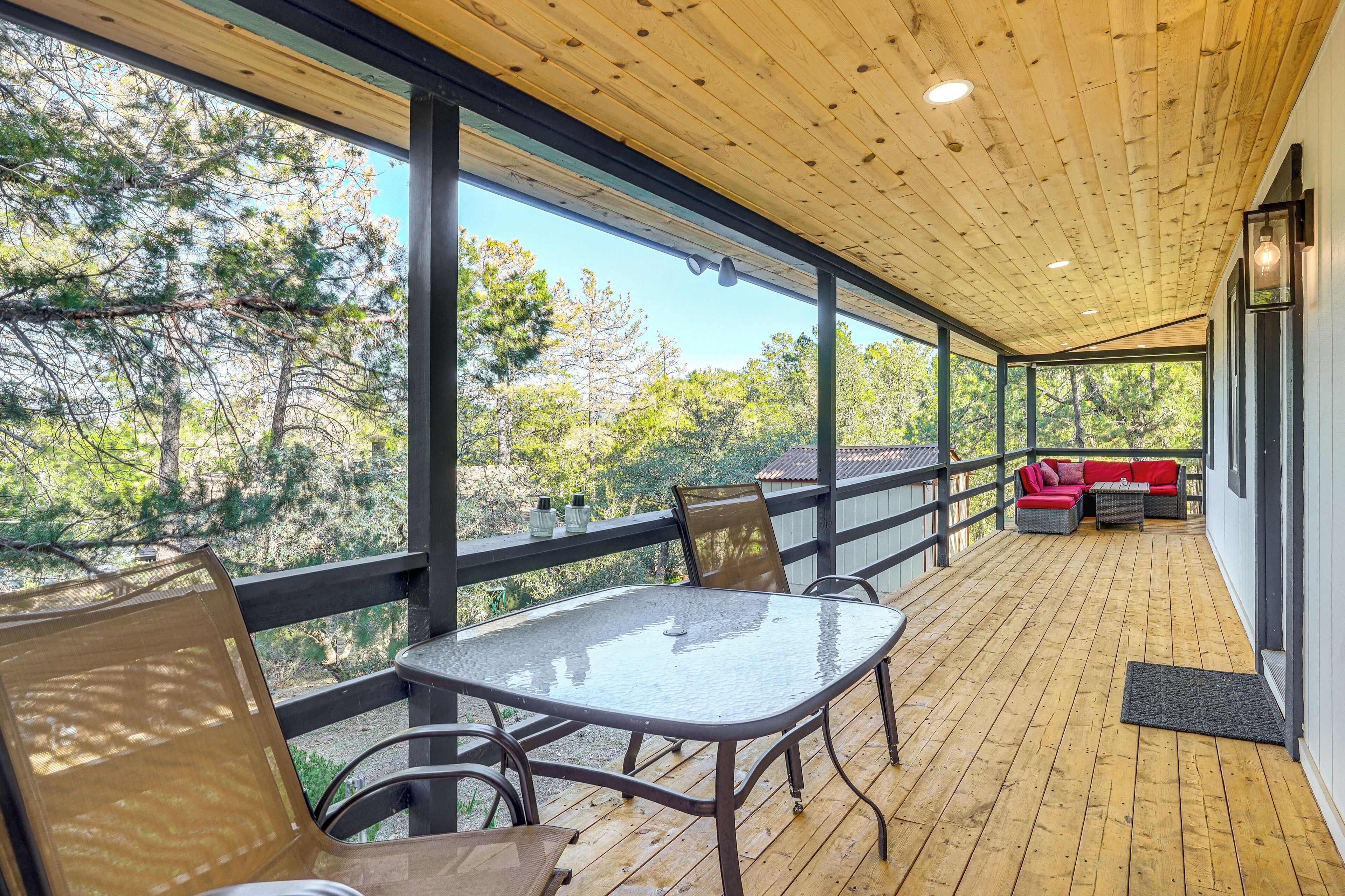A covered outdoor area with a table and chairs, a red sofa, and a view of trees.