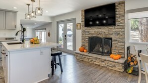 A modern kitchen with a stone fireplace, a large island, and a dining area with a view of the outdoors. - Relax Fireside: Prescott Retreat w/ Hot Tub! (Prescott)