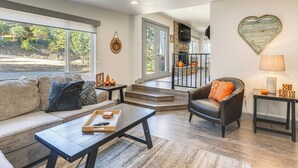 A spacious living room with a sofa, coffee table, and a fireplace. There is a staircase leading to an upper level. - Relax Fireside: Prescott Retreat w/ Hot Tub! (Prescott)