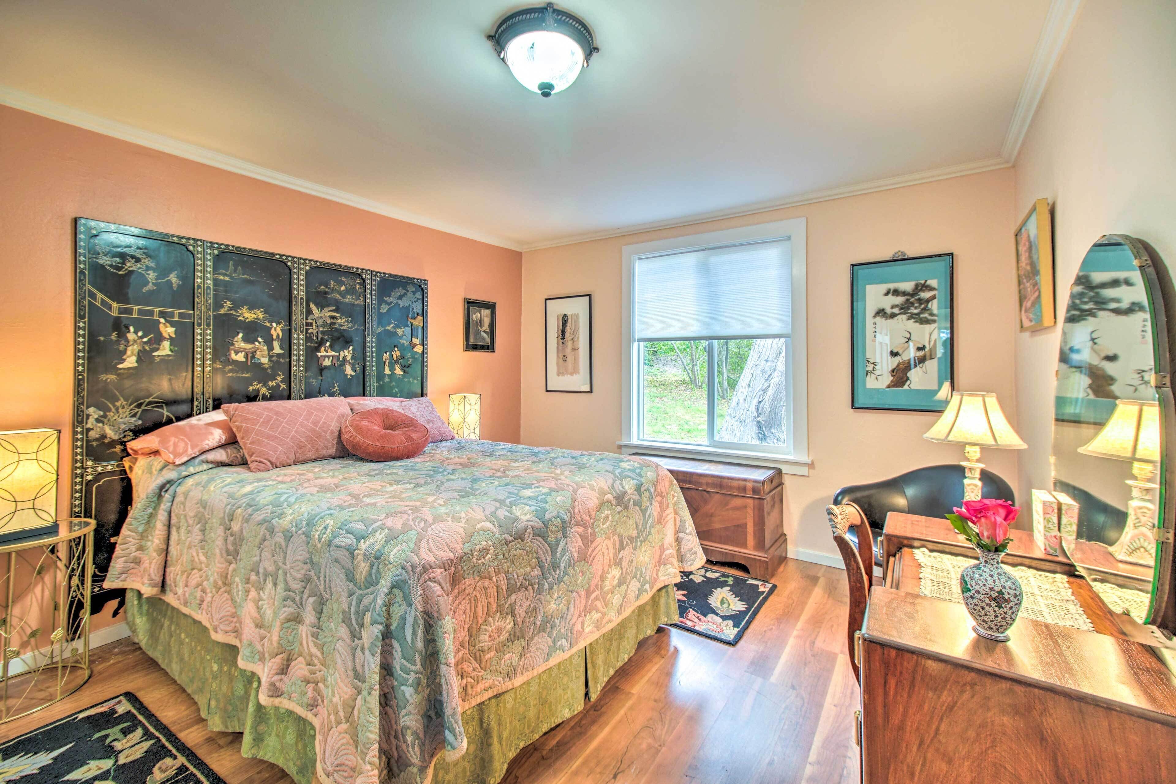 A bedroom with a large bed, a wooden desk, a chair, a window with blinds, and a ceiling light.