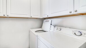 Un espace buanderie équipé d’un lave-linge et d’un sèche-linge à chargement frontal, de meubles blancs et d’un panneau de commande.