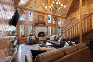 A log cabin interior with a stone fireplace, wooden walls, and a staircase. - Broken Bow Family Cabin w/ Private Hot Tub! (Broken Bow)