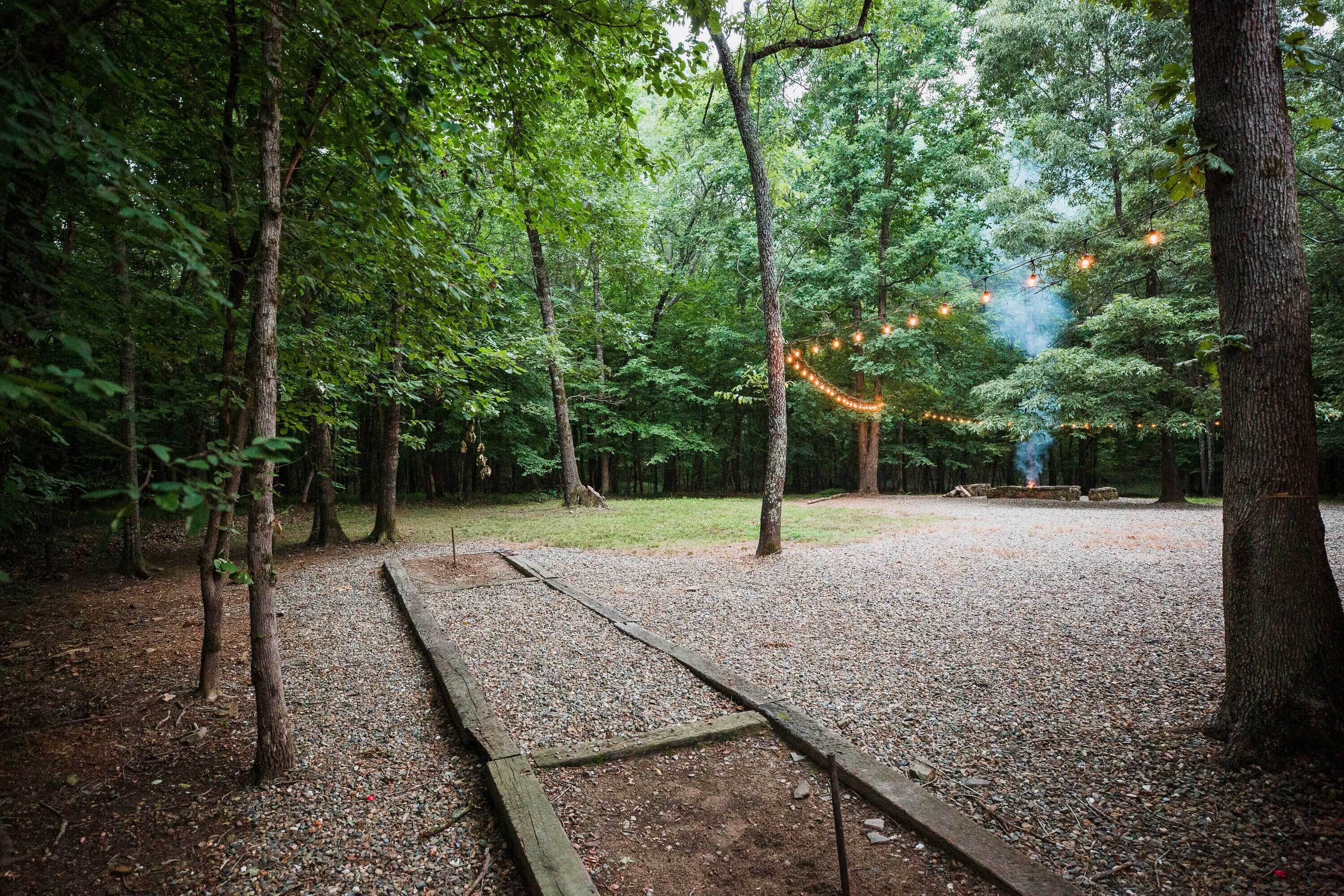 A forested area with a gravel path, wooden benches, and string lights.