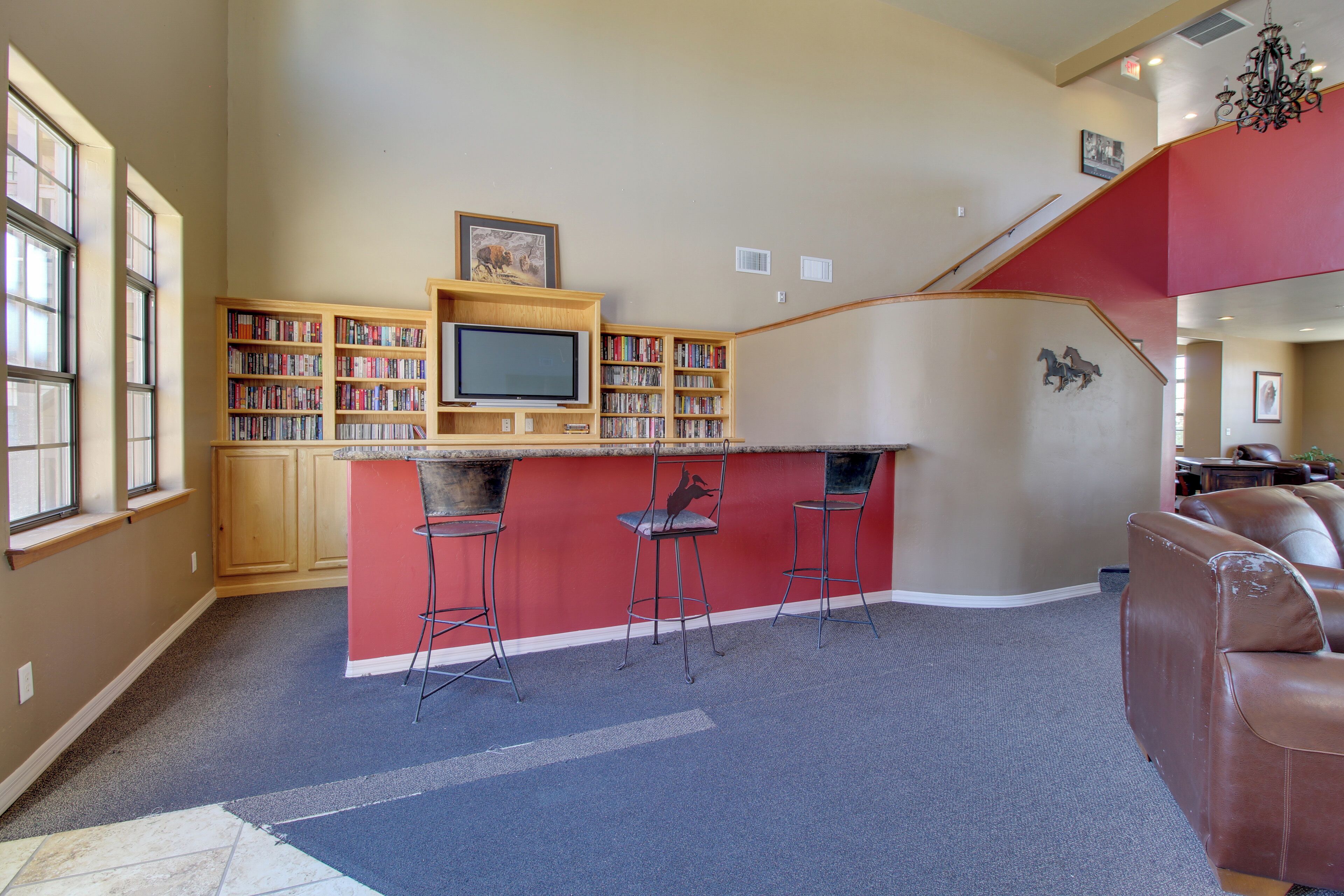 A home interior with a kitchen area, a bar with stools, a red accent wall, and a large leather couch.