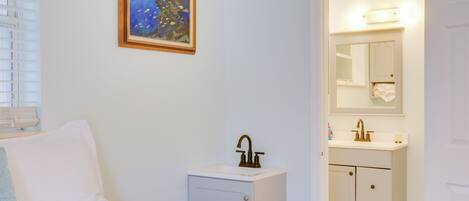 Un dormitorio con cama, mesita de noche, un cuadro y baño con lavabo y espejo.