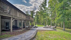 Een overdekt terras buiten, met stenen vloer, een zithoek met tafels en stoelen, en uitzicht op een bebost gebied.