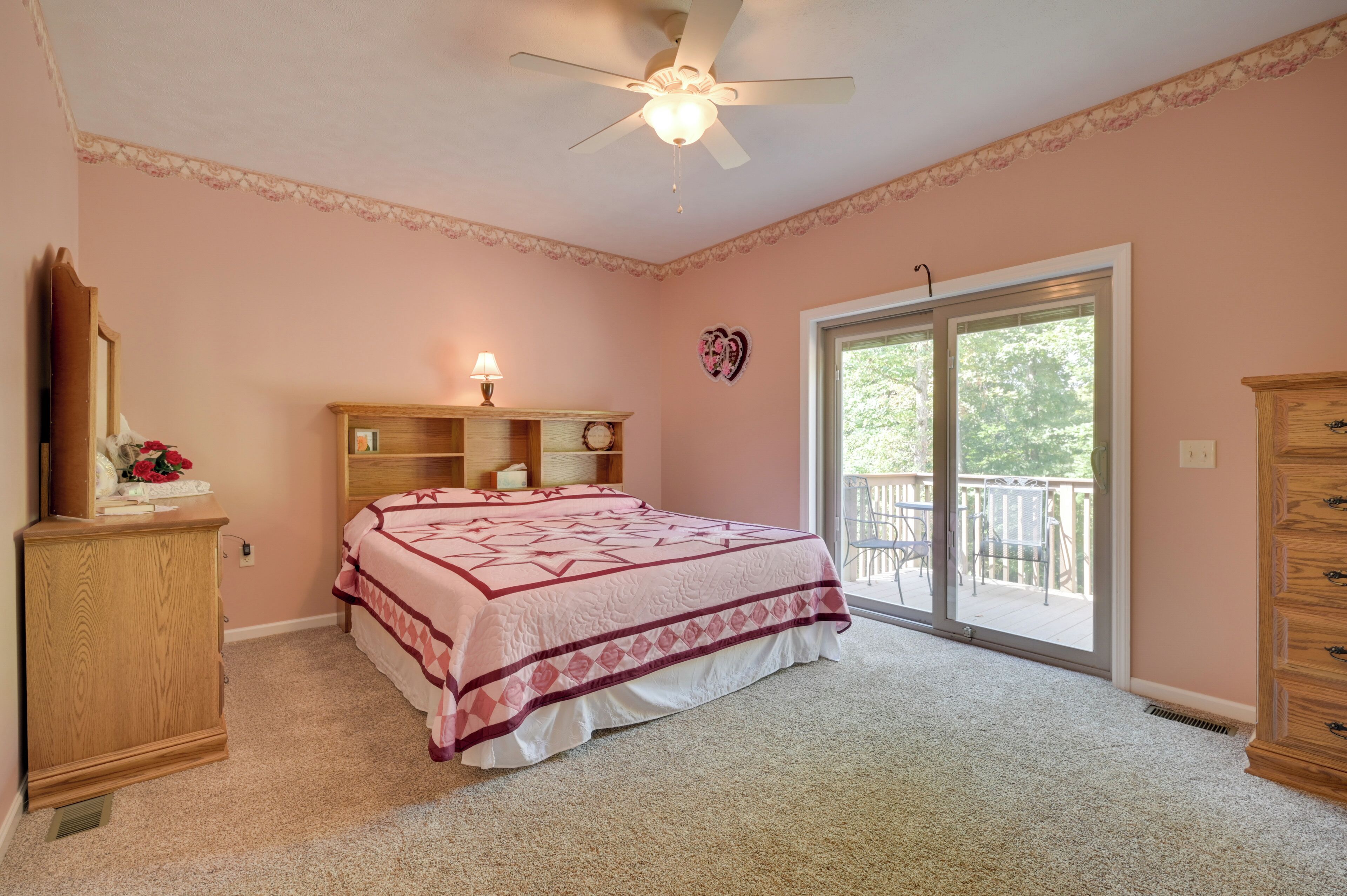 Ein Schlafzimmer mit Bett, Kommode, Nachttisch, Deckenventilator und einer Glastür, die auf einen Balkon führt.