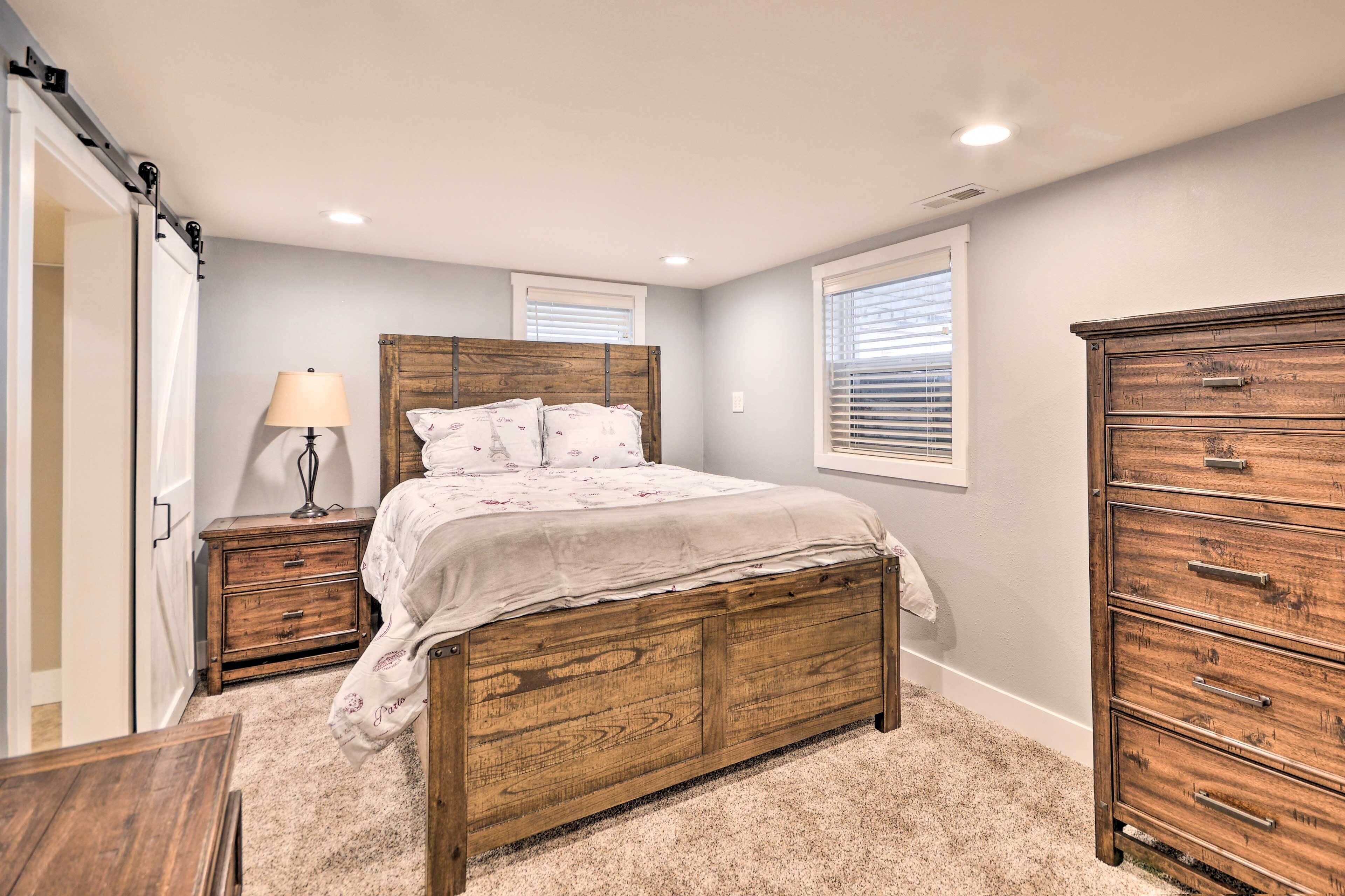 A bedroom with a wooden bed, a nightstand, a dresser, and a window with blinds.