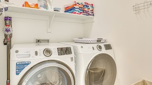 A laundry area with two front-loading washing machines, a shelf with folded towels, and a hanging rack. - Families Welcome: Phoenix Home w/ Backyard Oasis (Phoenix)