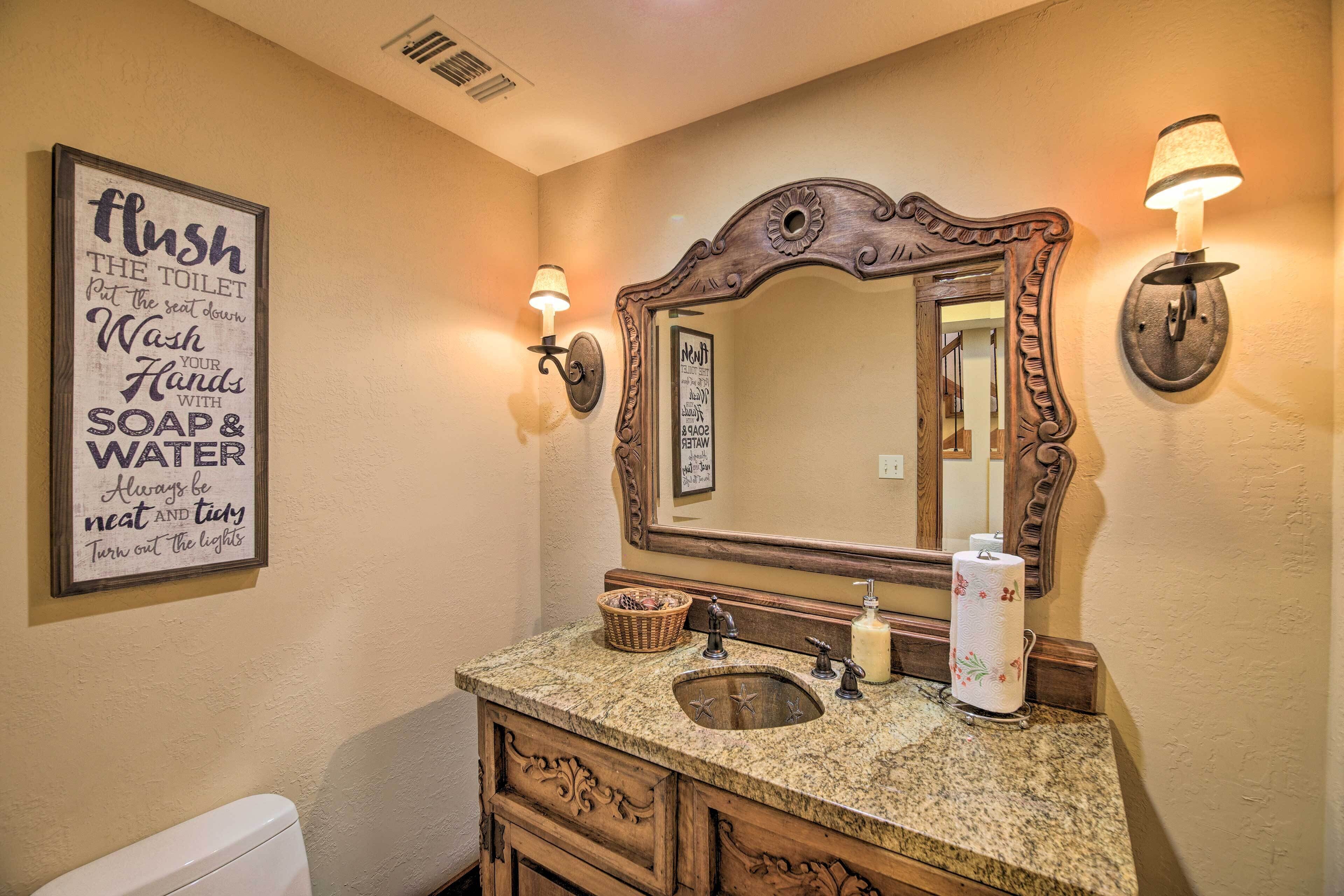 A bathroom with a sink, mirror, and wall-mounted lights. There is a sign on the wall with hygiene instructions.