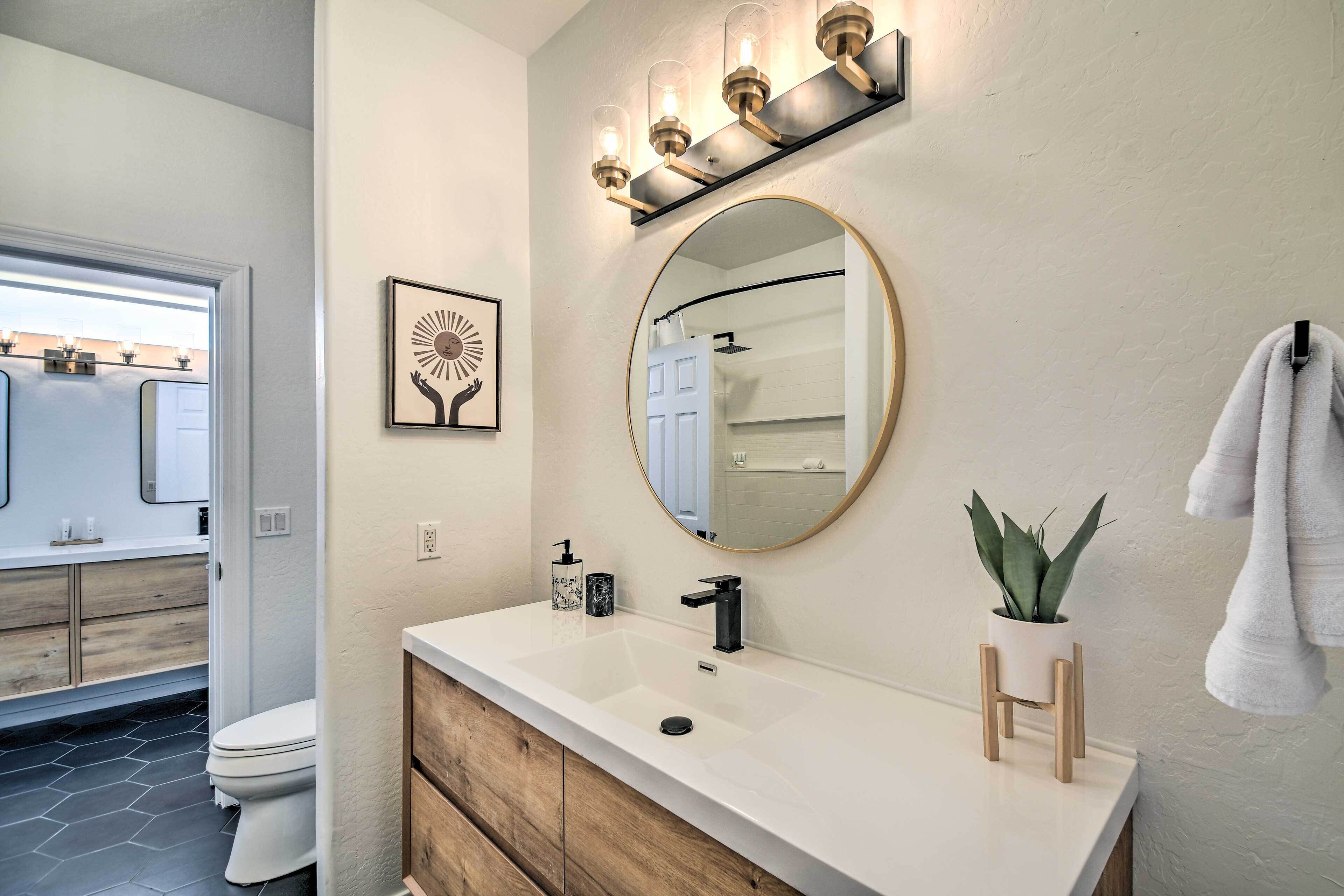 A bathroom with a white vanity, a round mirror, a black faucet, and a potted plant.