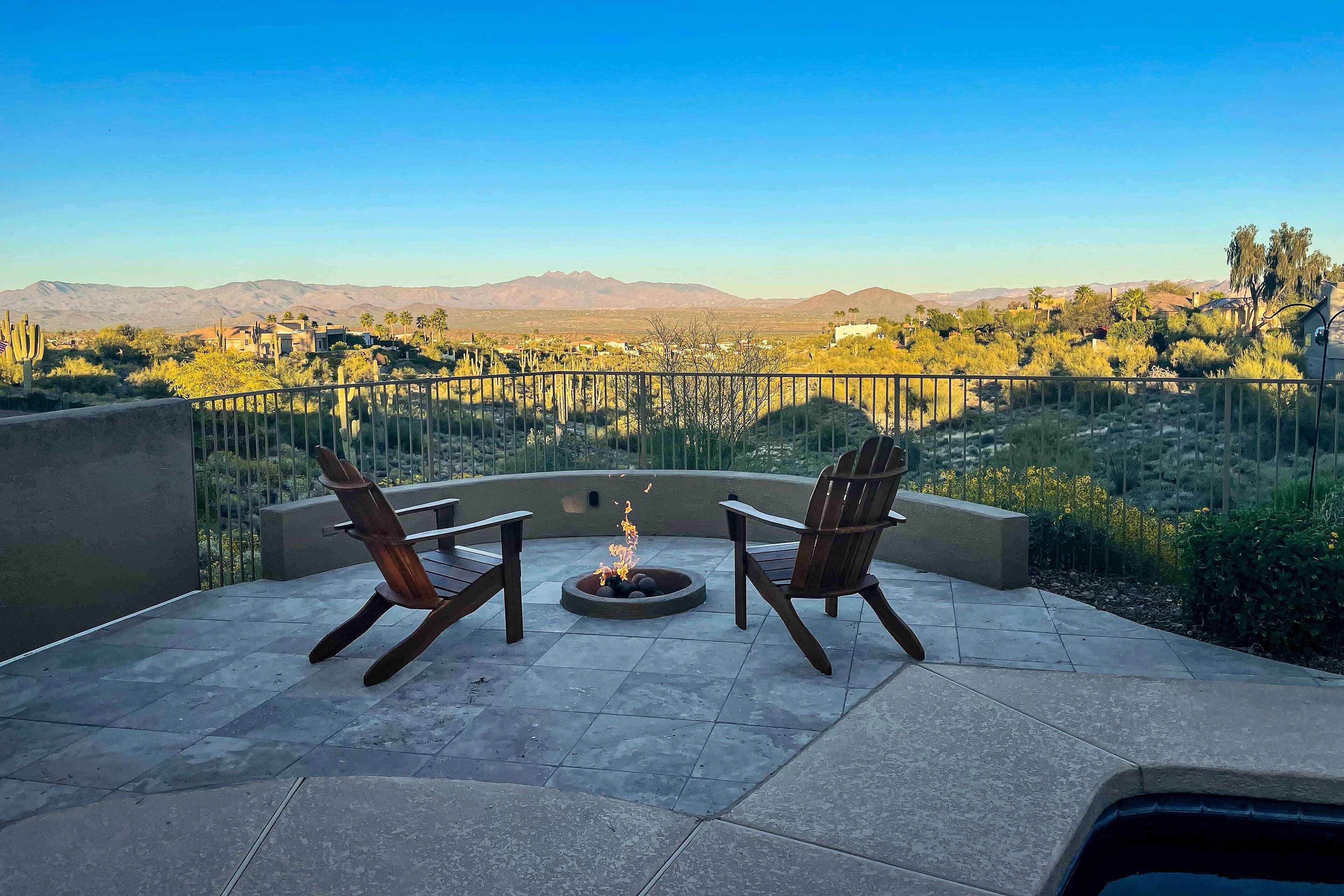 Un patio con dos sillas de madera y un hogar para fuego, con vistas a un paisaje desértico y montañas.