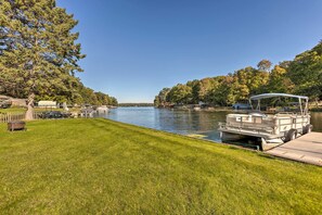 A lakeside dock with a boat, grassy banks, and trees. - Lakefront Ludington Retreat w/ Kayaks & Fire Pit! (Ludington)