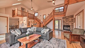 A spacious living room with a large gray sectional sofa, wooden coffee table, and a fireplace. A wooden staircase with a railing leads to an upper level. - Hot Tub & Mtn View: Dog-friendly Payson Getaway! (Payson)
