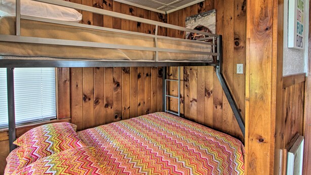 Un lit superposé avec une couverture aux motifs colorés en zigzag, des murs en bois et une échelle menant au lit supérieur.