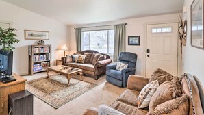 A living room with a sofa, armchair, coffee table, bookshelf, and a television. - New! Kalispell House w/ Grill < 35 Mi to Glacier! (Kalispell)