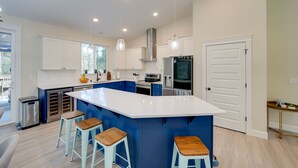 Een moderne keuken met een ruim eiland, blauwe kastjes, roestvrijstalen apparatuur en hangende lampen.