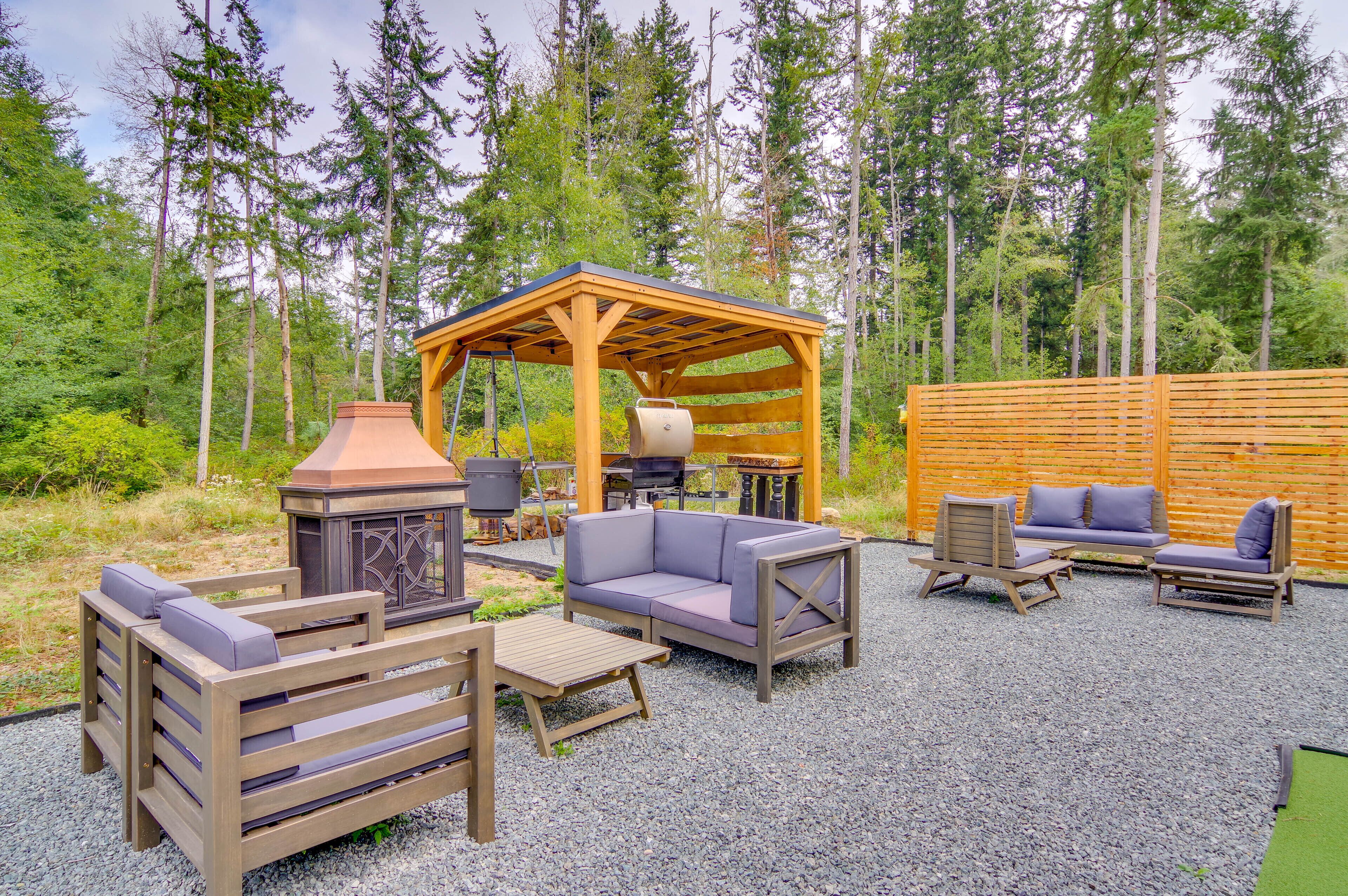 Eine Terrasse im Freien mit überdachter Sitzgruppe, einem Grill und einem Holztisch.