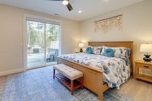 Een slaapkamer met een groot bed, een bankje, een houten nachtkastje en uitzicht op de natuur door een schuifpui.