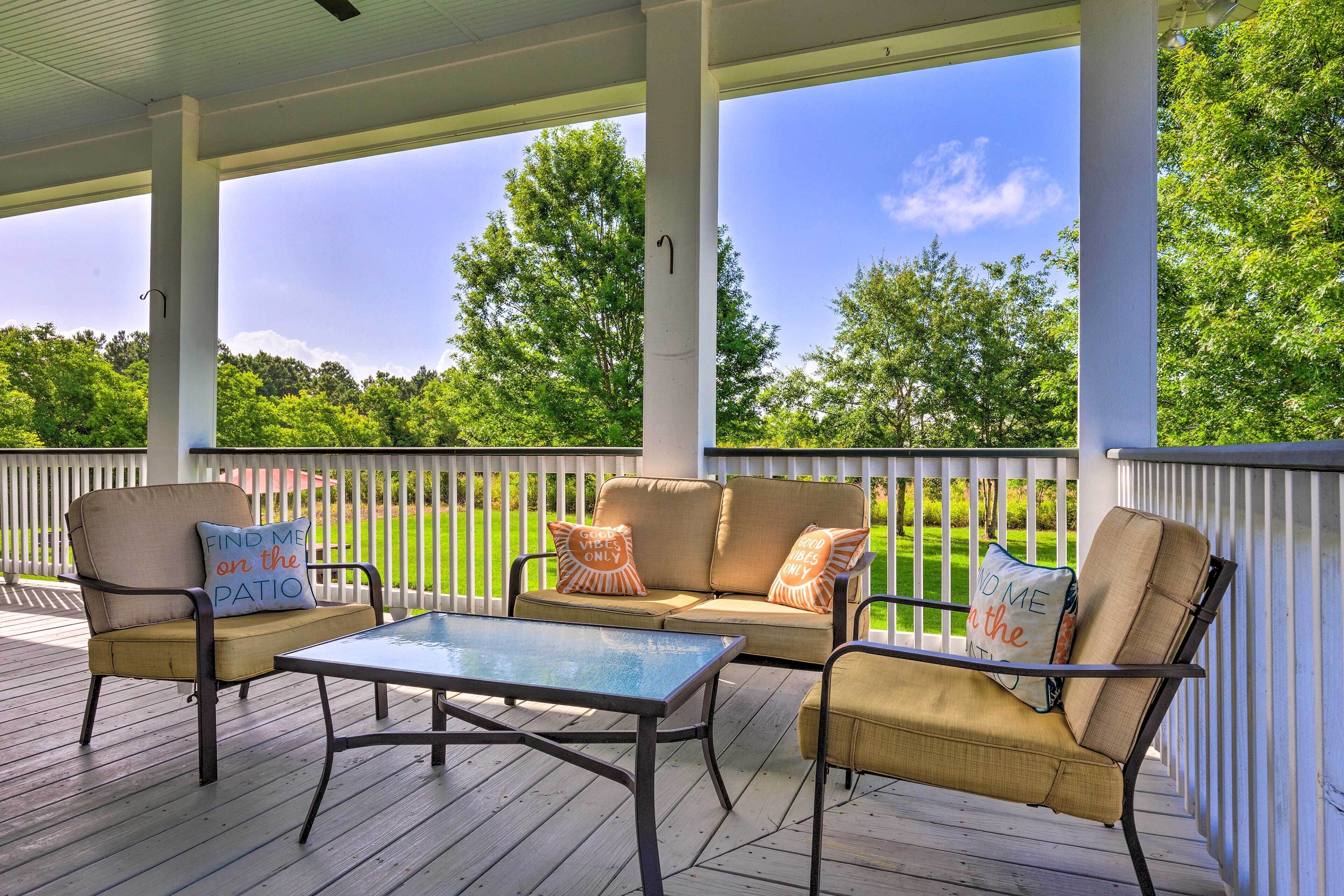 A covered outdoor seating area with a table and two sofas, each with a cushion.