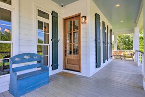 A porch with a wooden bench, a wooden door, and a bench with cushions in the background. - Bright Waveland Home - Walk to Beach Access! (Waveland)