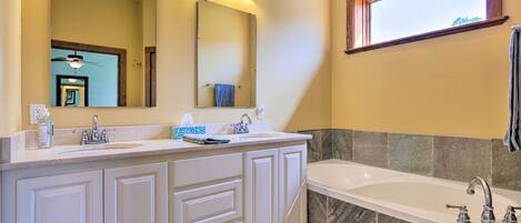 A bathroom with a double sink vanity, a large mirror, a bathtub, and a window.