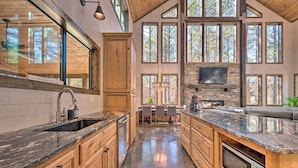 Cocina amplia con armarios de madera, encimeras de granito y grandes ventanales con vistas a árboles.