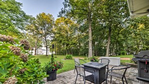 A patio with a table and chairs, surrounded by potted plants and trees. - Charming Lakefront Home w/ Grill & Fire Pit! (New Concord)