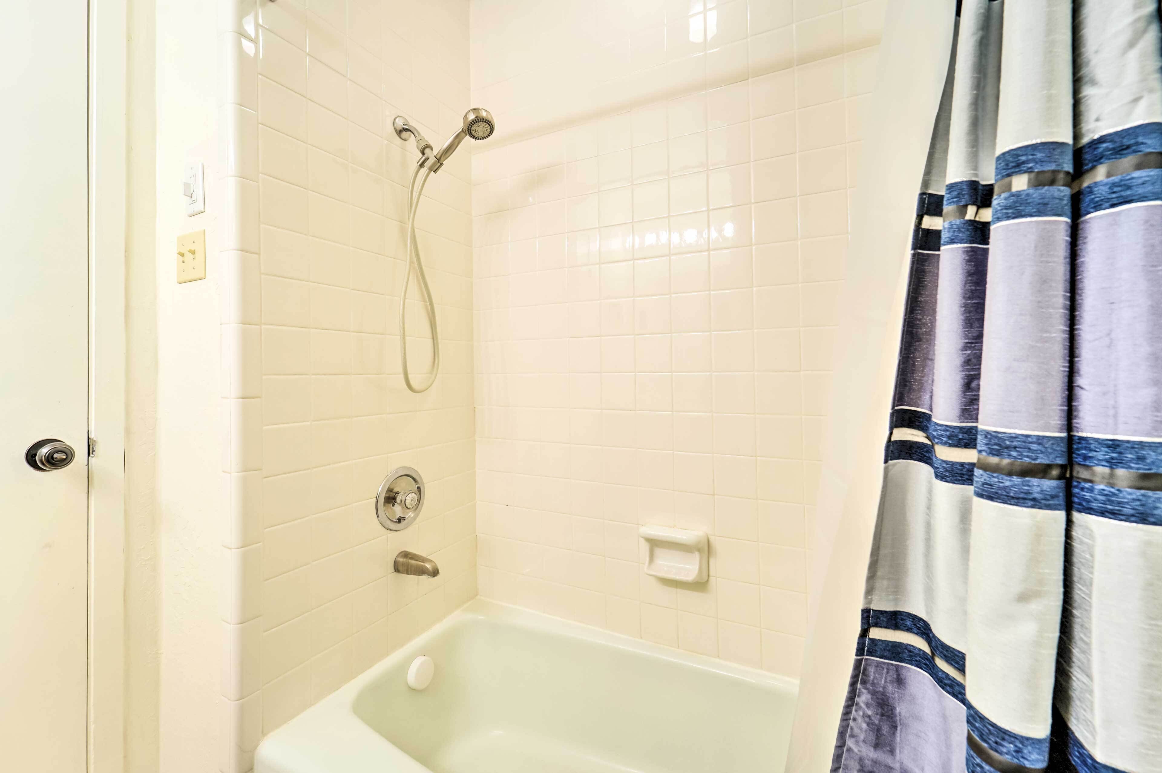 A bathroom with white tiled walls, a bathtub, a showerhead, and a striped curtain.