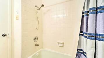 A bathroom with white tiled walls, a bathtub, a showerhead, and a striped curtain.