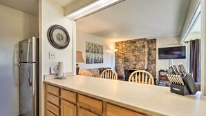 A kitchen with a refrigerator, wooden cabinets, a clock, a stone wall, a TV, and a knife block. - Slope Side Durango Condo at Purgatory Resort! (Durango)