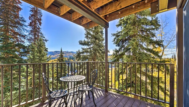 A wooden deck with a table and chairs, overlooking a forested area with mountains in the distance. - Slope Side Durango Condo at Purgatory Resort! (Durango)