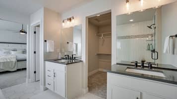 A modern bathroom with a large mirror, two sinks, and a shower area.