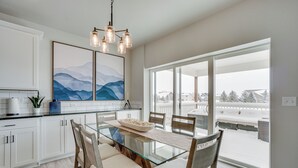A modern kitchen with a glass dining table, white cabinets, and a large window with a view of a snowy landscape.