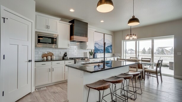 A modern kitchen with white cabinets, a stainless steel microwave, a built-in stove, and a large island with bar stools.