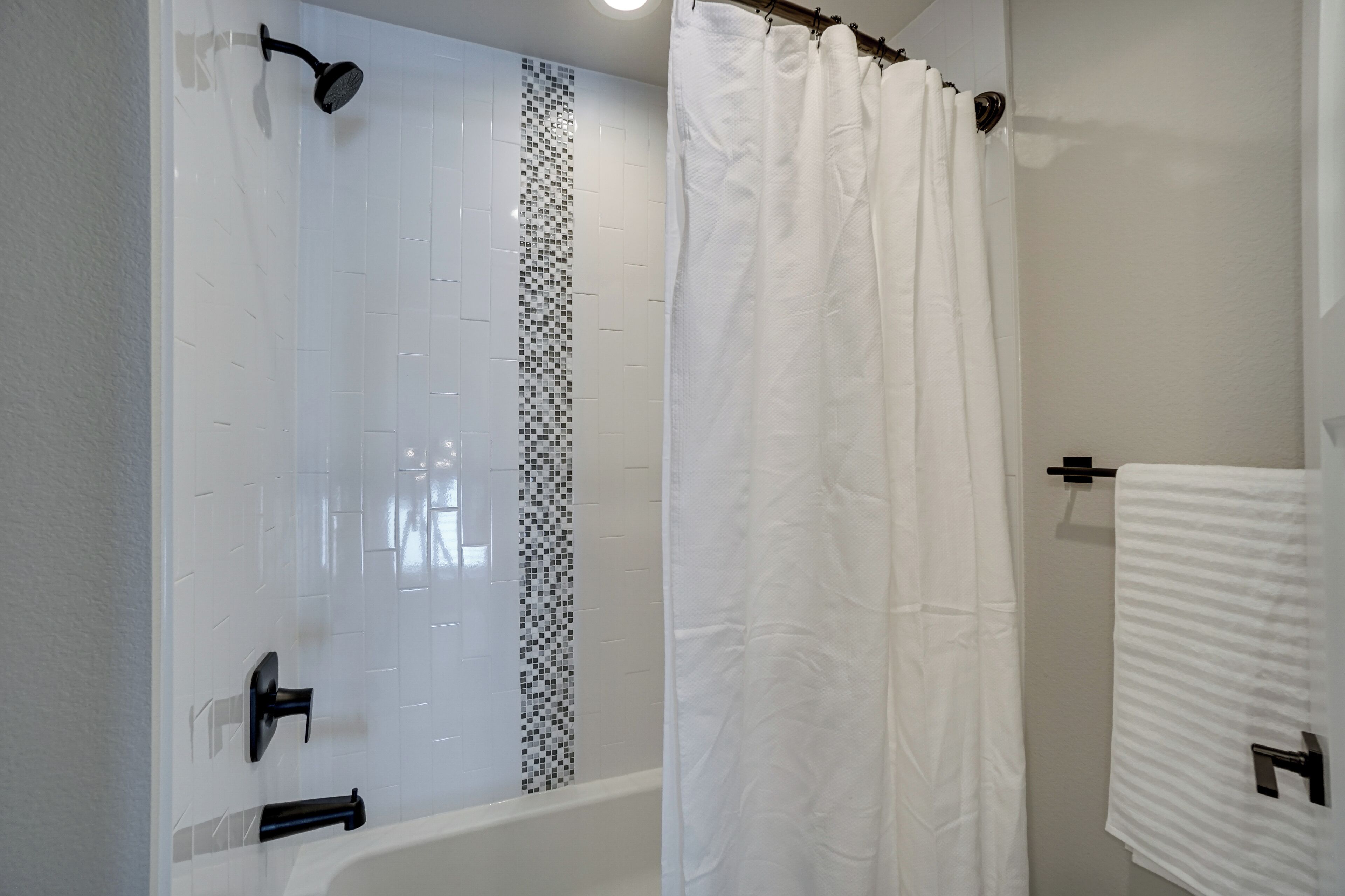 A modern bathroom with a shower, a bathtub, and a white tiled wall.