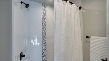 A modern bathroom with a shower, a bathtub, and a white tiled wall.