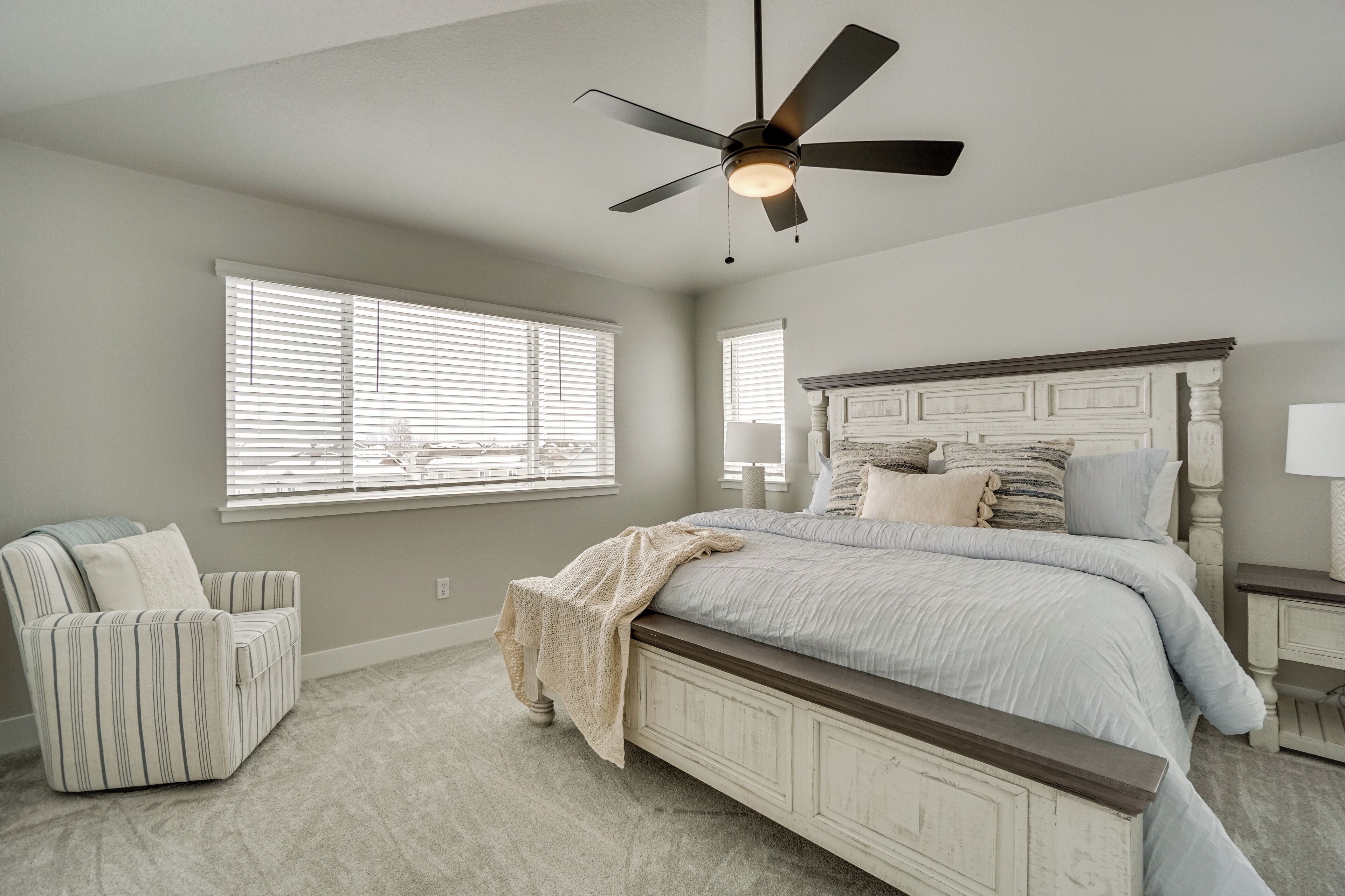 Une chambre à coucher avec un lit, une chaise, un ventilateur de plafond et une fenêtre avec des stores.