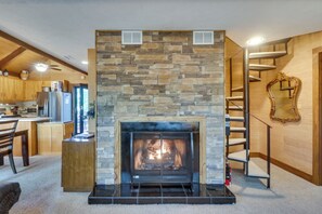 Ein Kamin aus Stein mit modernem Design, eine Holztreppe und ein Küchenbereich mit Holzausstattung und Geräten.
